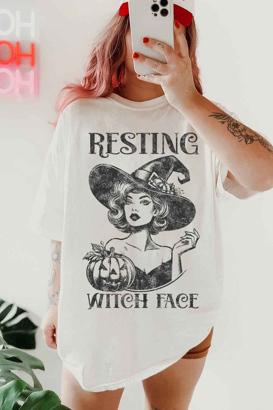 Young woman wearing an oversized white t-shirt with a Halloween-themed design of a witch and pumpkin that reads, “RESTING WITCH FACE.”