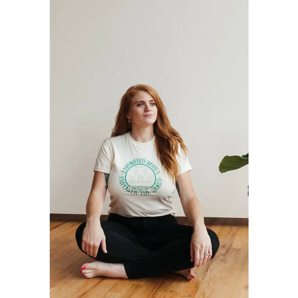 Model seated wearing a white t-shirt with teal text that form a circle that reads “ empowered women empower the world.”