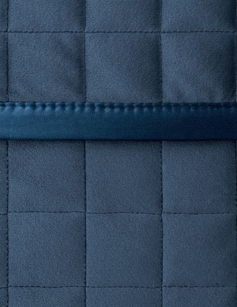 Close up blue, velvet, quilted bedding with satin edge.