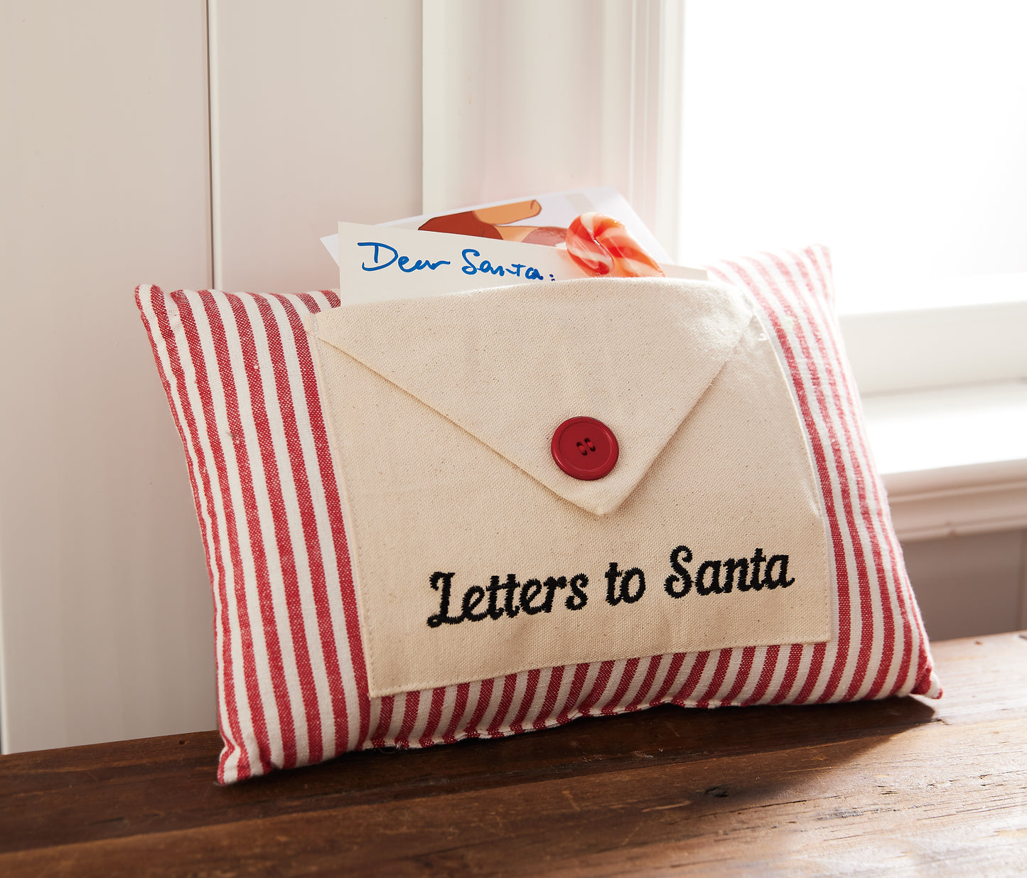 Red and white striped pillow with envelope design for holding letters to Santa seated near bedroom window