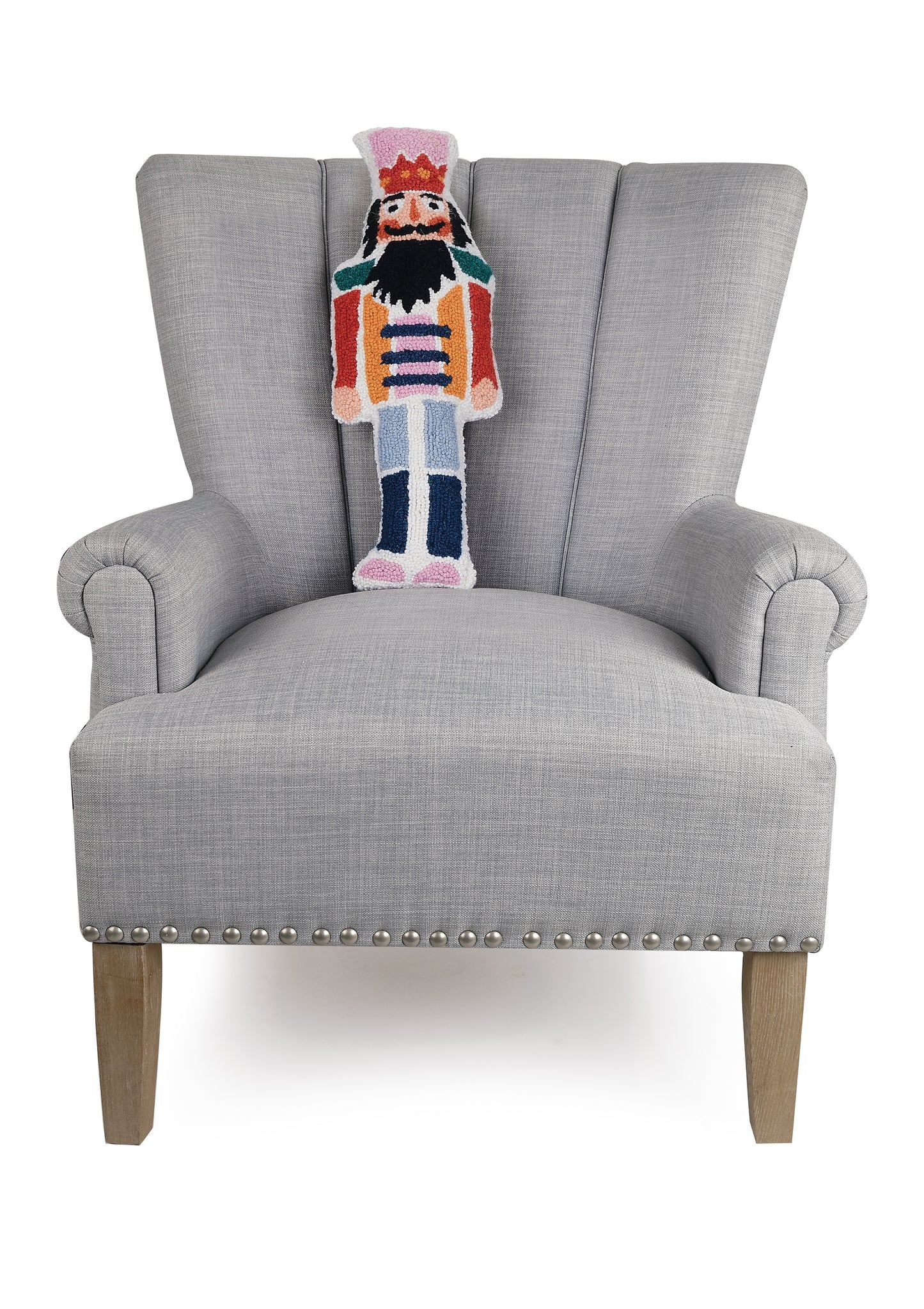 Multicolored wool hooked pillow shaped like the Nutcracker displayed in gray sitting chair.