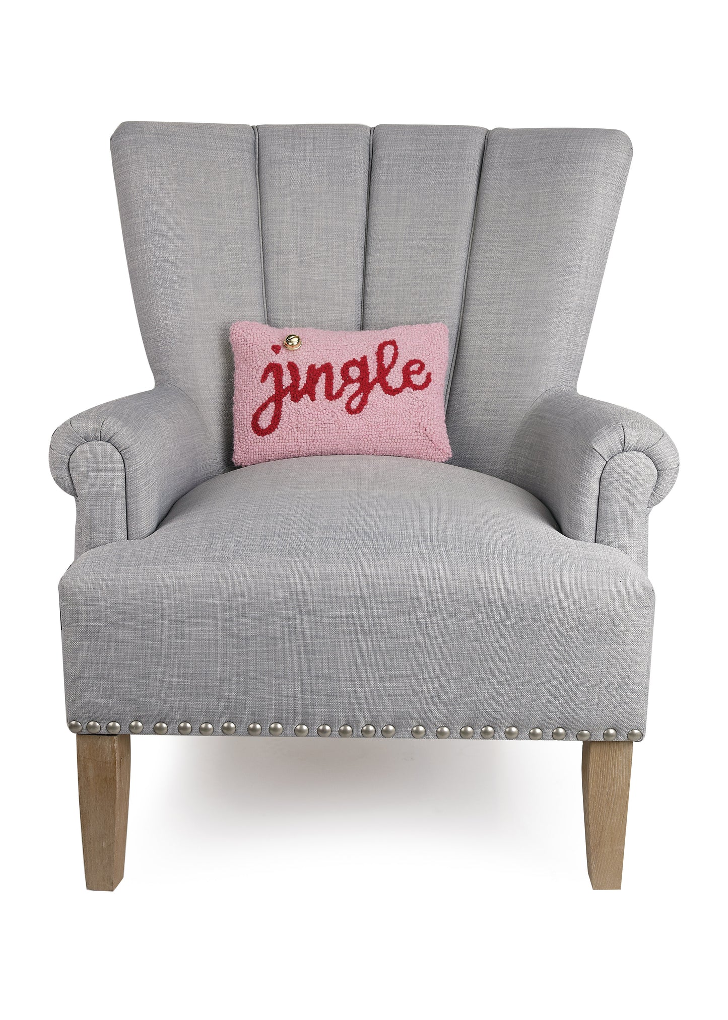 Gray chair showcasing pink wool “jingle” pillow with red cursive letters and gold bell accent over the “i”