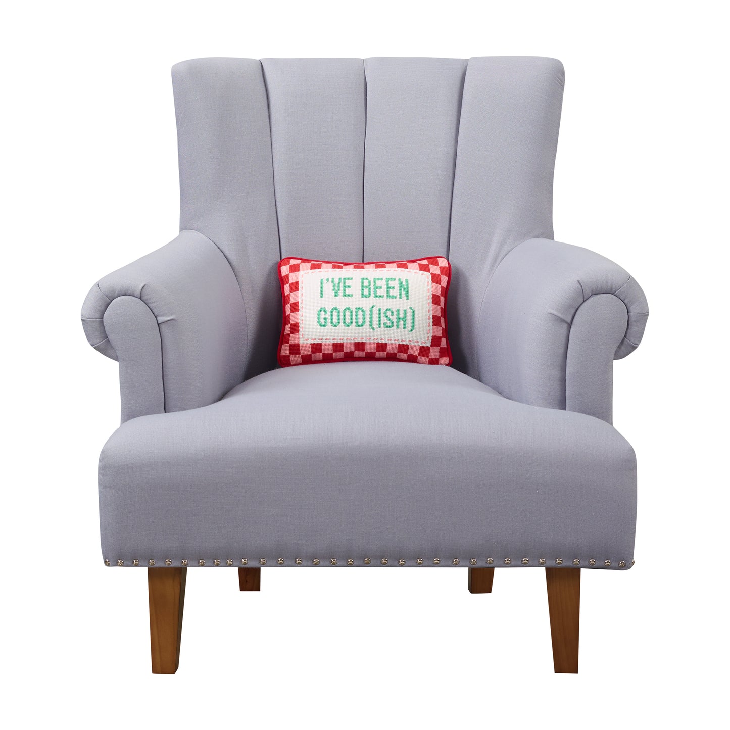 Gray chair showcasing needlepoint holiday pillow with red and pink checkered frame that reads, “I’ve been good(ish)” in green letters.