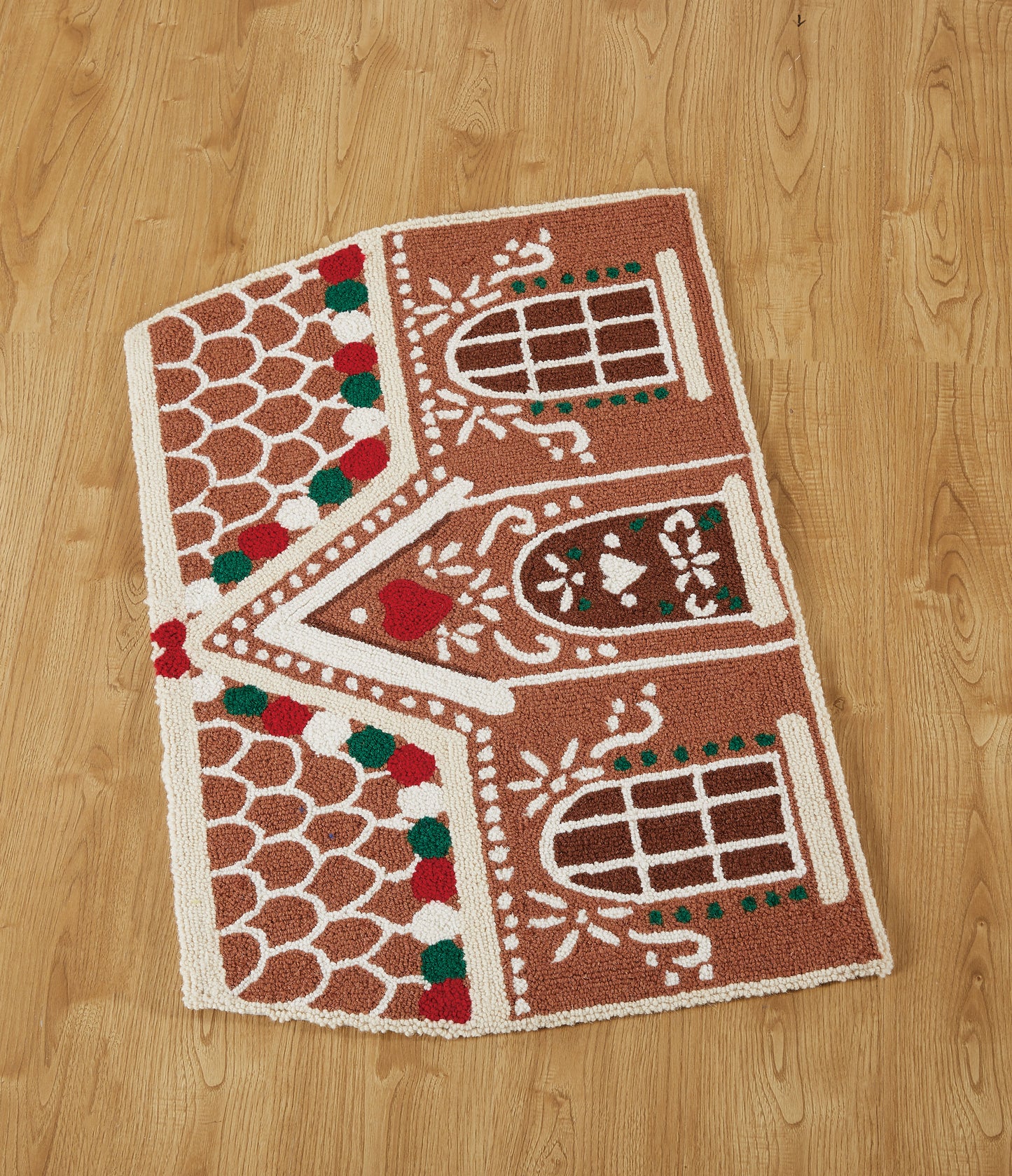 Floor view of wool gingerbread house rug made of wool with red, white and green dotted trim