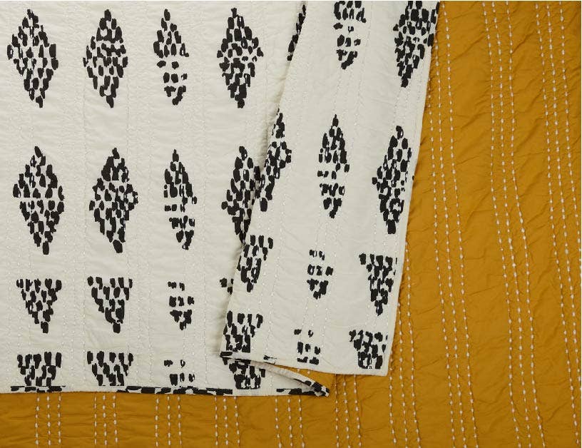 Detailed view of reversible quilt with black dotted diamond design against a cream spread