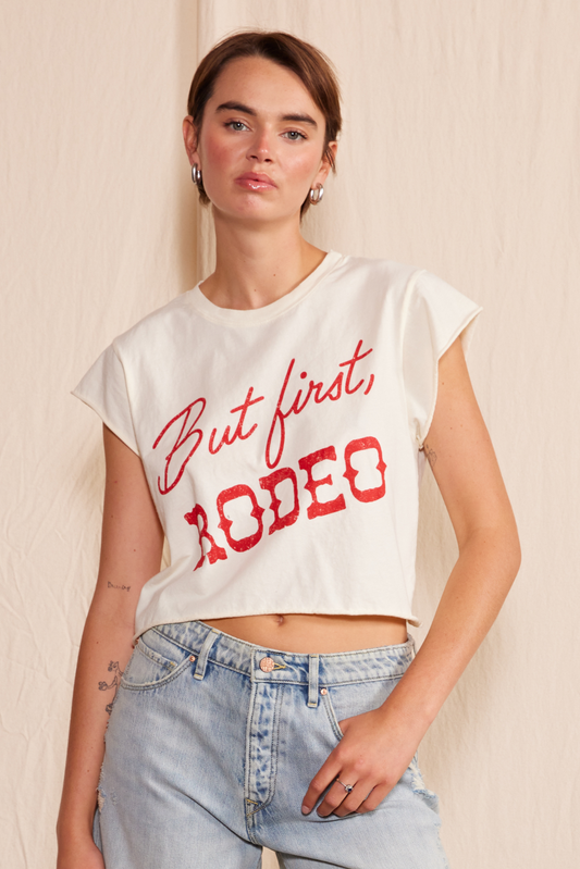 Natural colored cropped top with the flowy sleeves and fun text that reads, “But first, rodeo” in red.