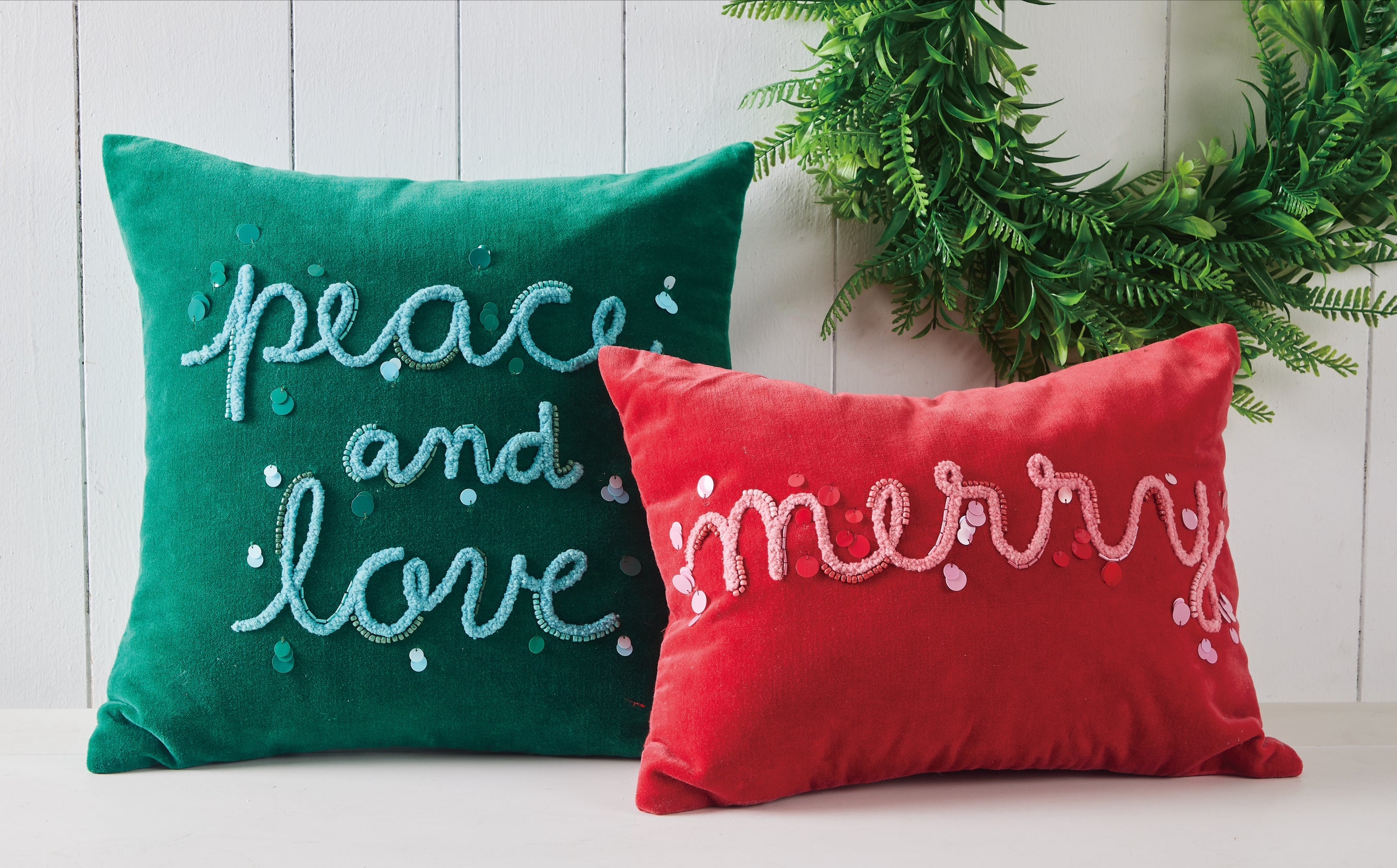 Green embroidered “peace and love” and red “merry” pillow set styled with Christmas wreath