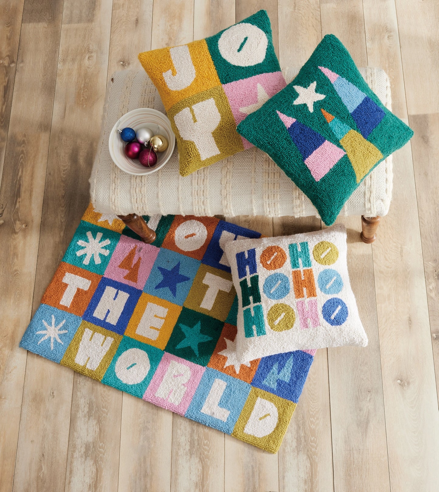 Holiday “joy to the world” rug and pillow spread on fabric stool with coordinating pillows, including the color block ho ho ho pillow