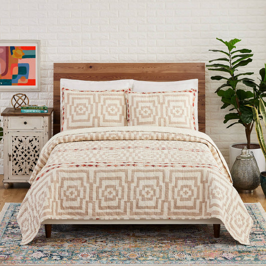 Multi-colored quilt with Greek key inspired design in light brown and red diamond strips on a cream colored spread 