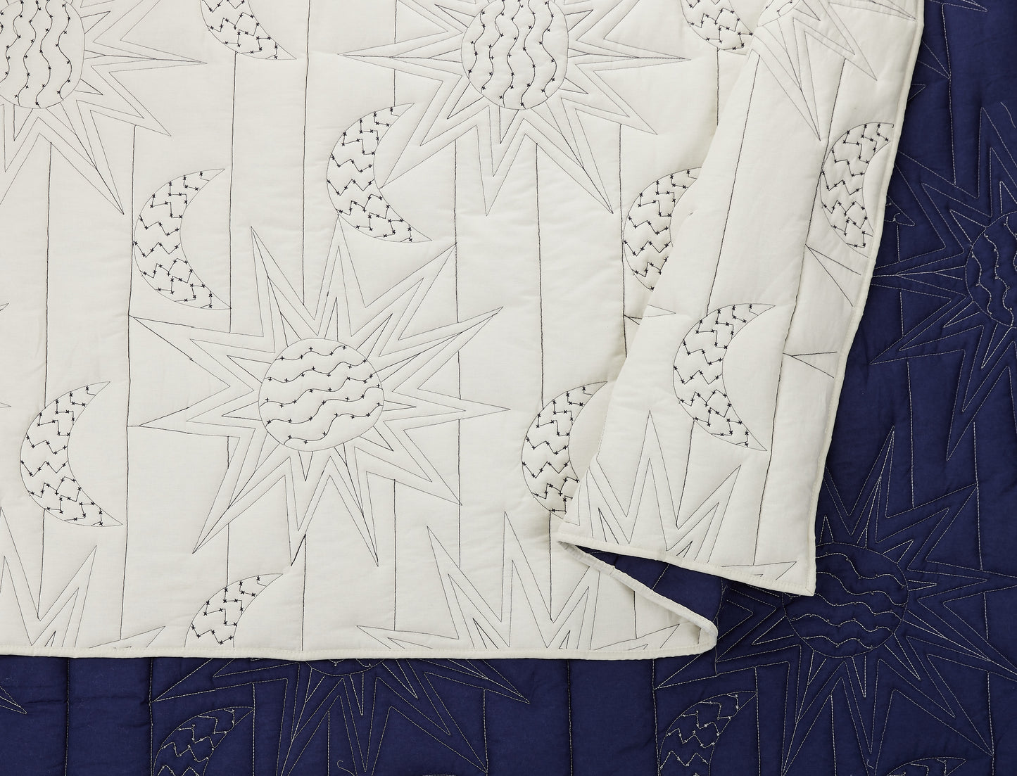 Detailed view of reversible quilt with elaborate stitching design adorned with staggered suns and moons