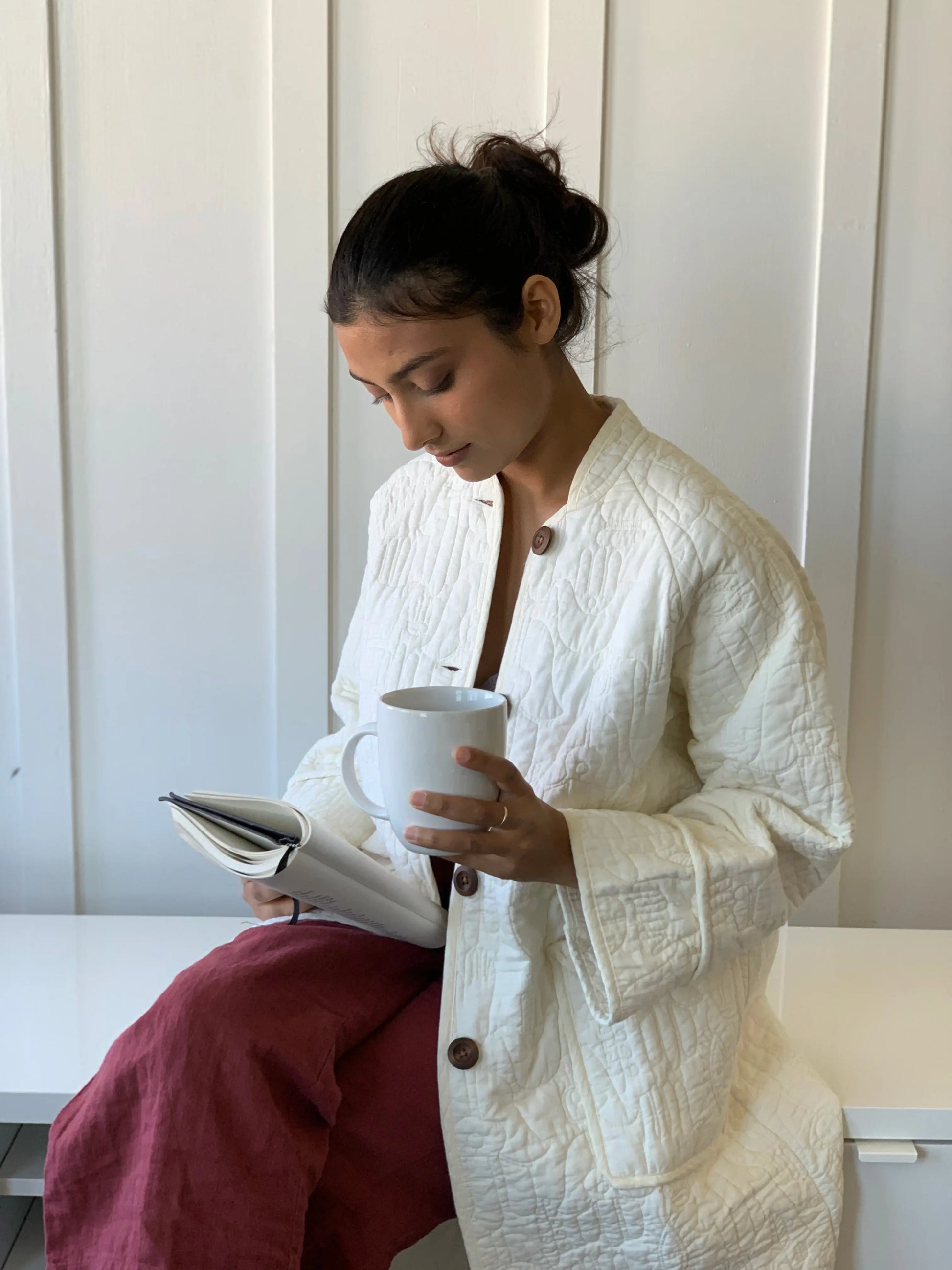 Woman reading and lounging while wearing embroidered house robe by Justina Blakeney.