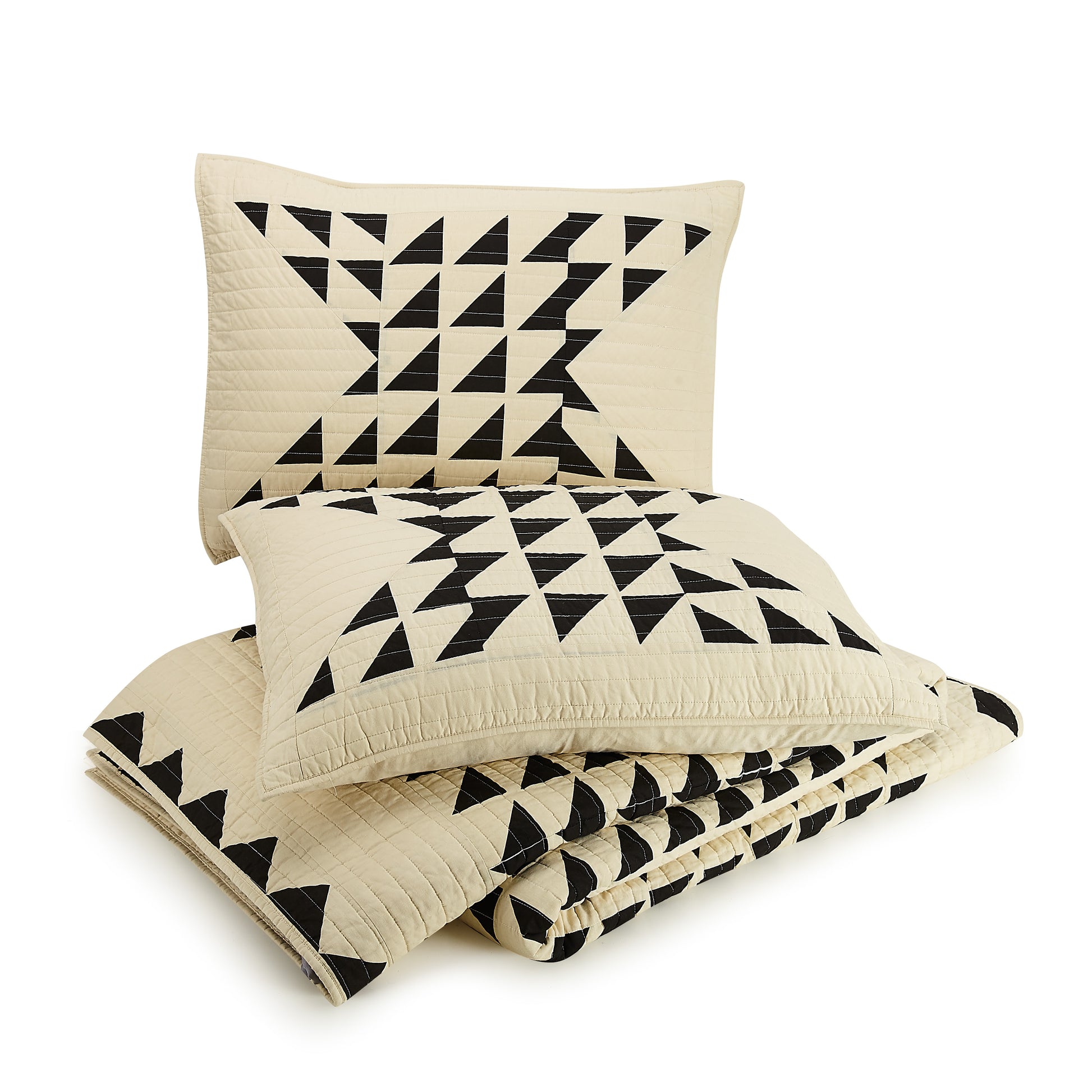 Matching pillows atop folded geometric, black and ivory quilt by Lemieux Et Cie