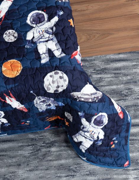 Detailed view of bed corner featuring kid’s bedding with planetary and galactic objects.