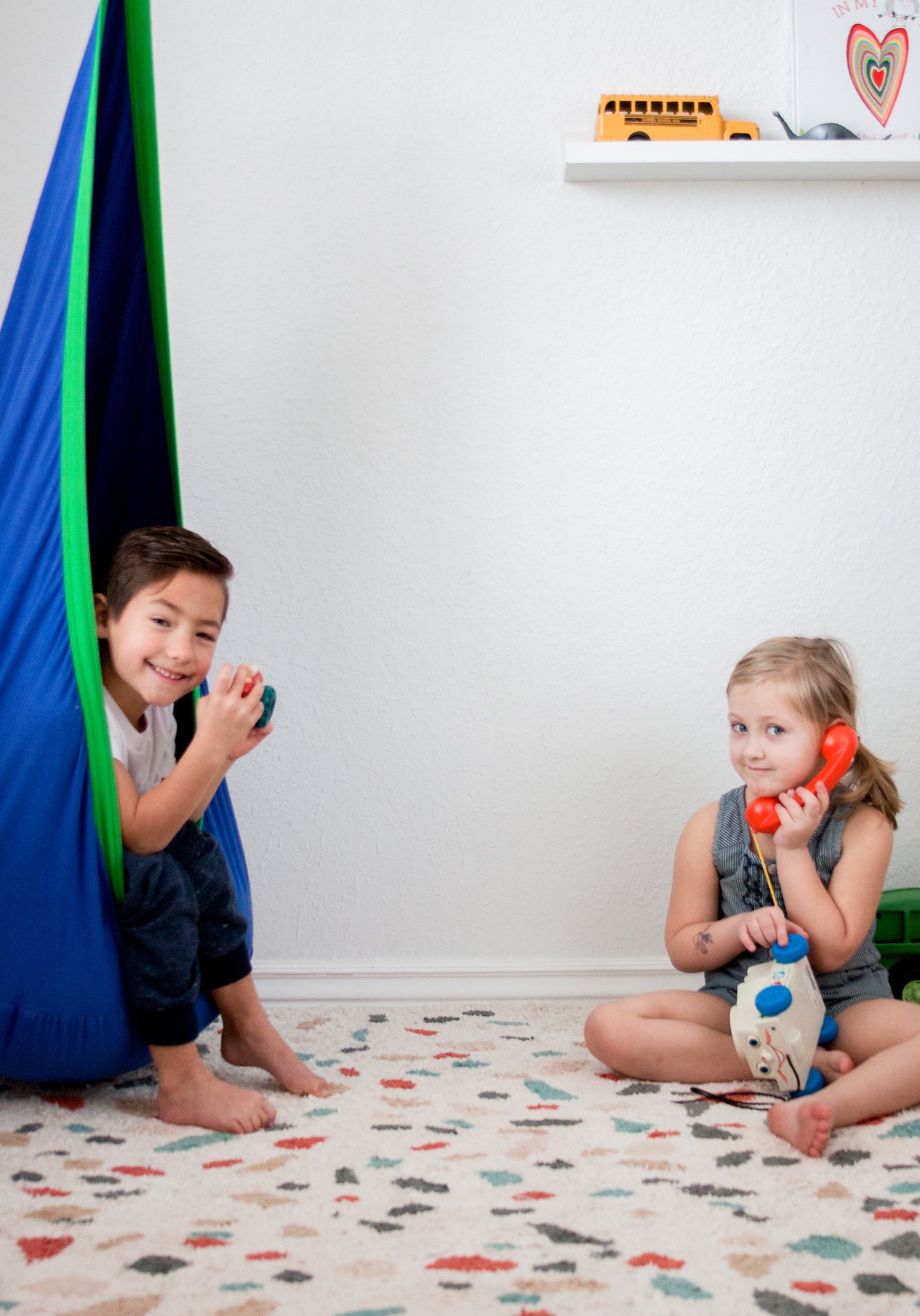 Kids in playroom featuring calming, indoor therapy swing in blue with green trim.