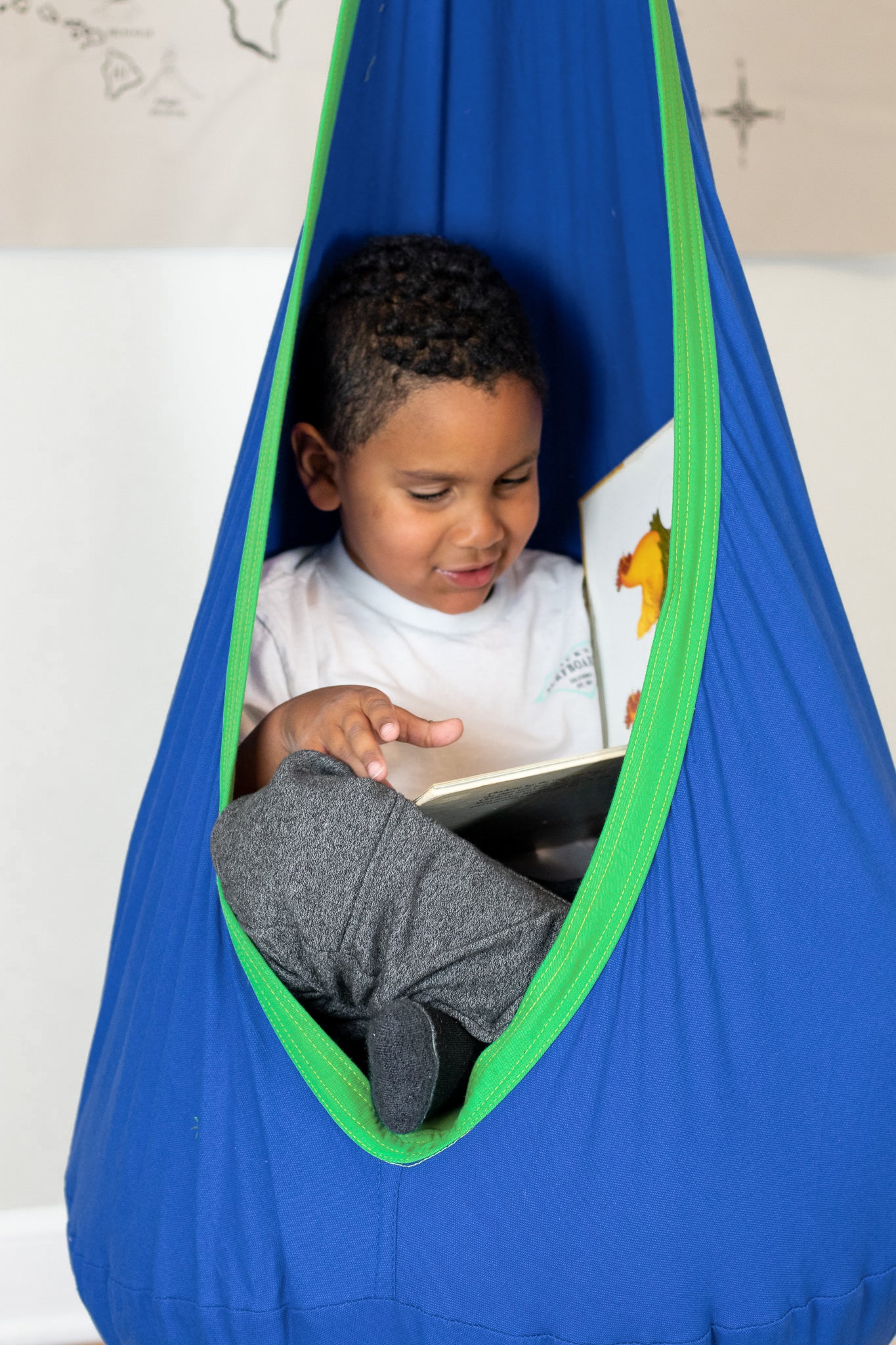 Young boy, earnestly reading, in Calming Cove Sensory Swing with blue base and bright green trim.