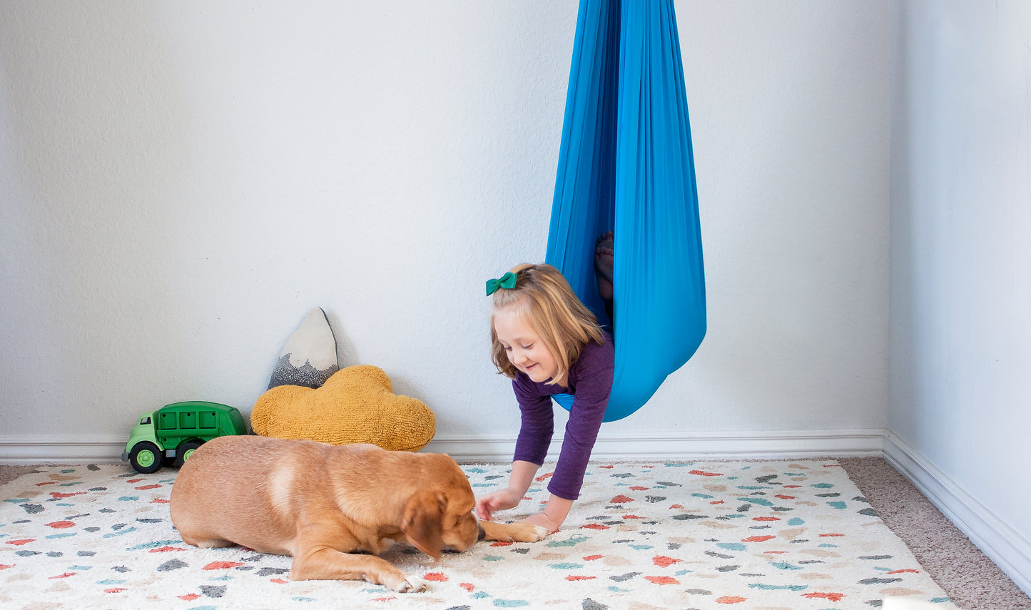 Young girl enjoying stretchy compression swing with Golden Retriever by her side.