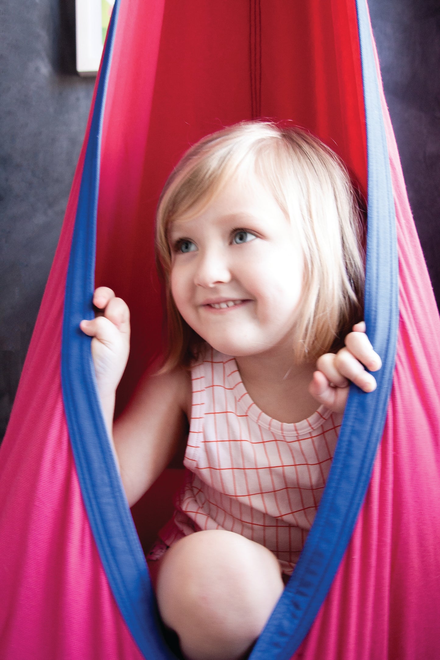 Young girl nestled in cozy pink and blue indoor therapy swing.