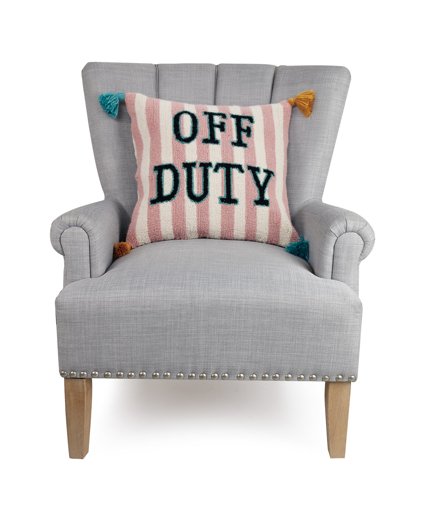 Yvonne Ellen pink and white striped, “Off Duty” throw pillow with green and yellow tassels against gray upholstered chair.