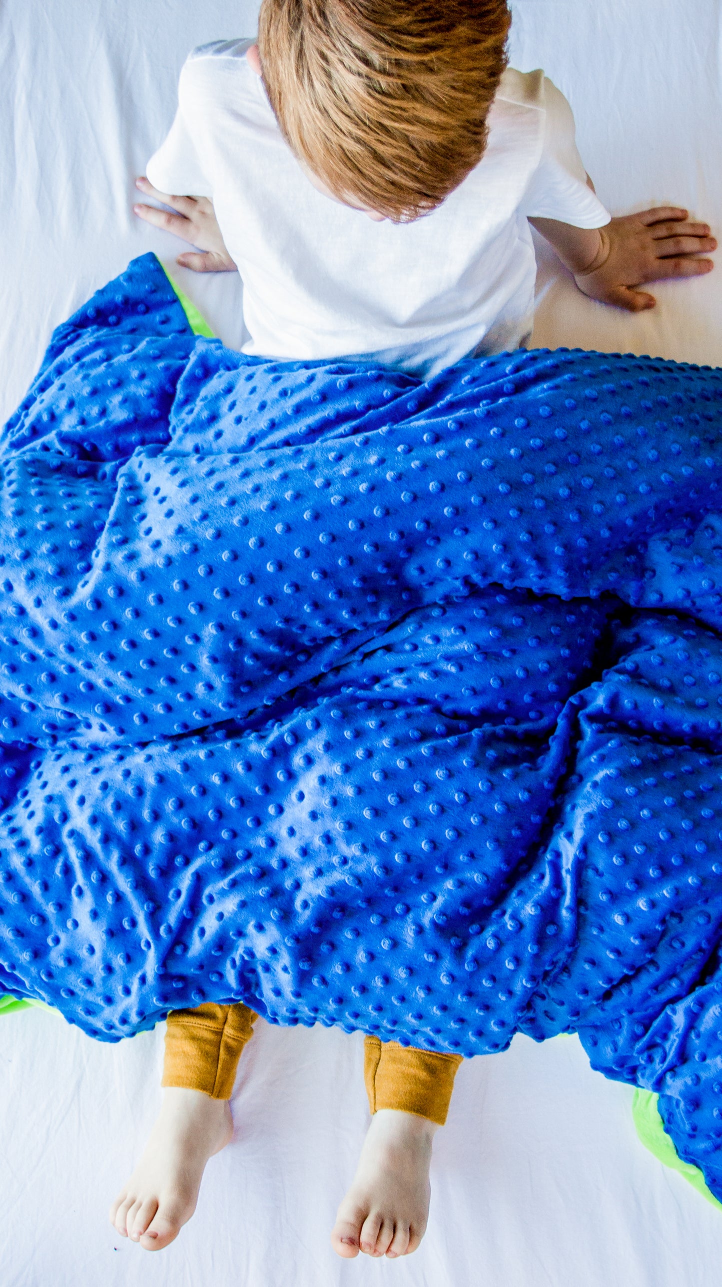 Boy relaxing under sensory weighted blanket with minky blue/green fabric.