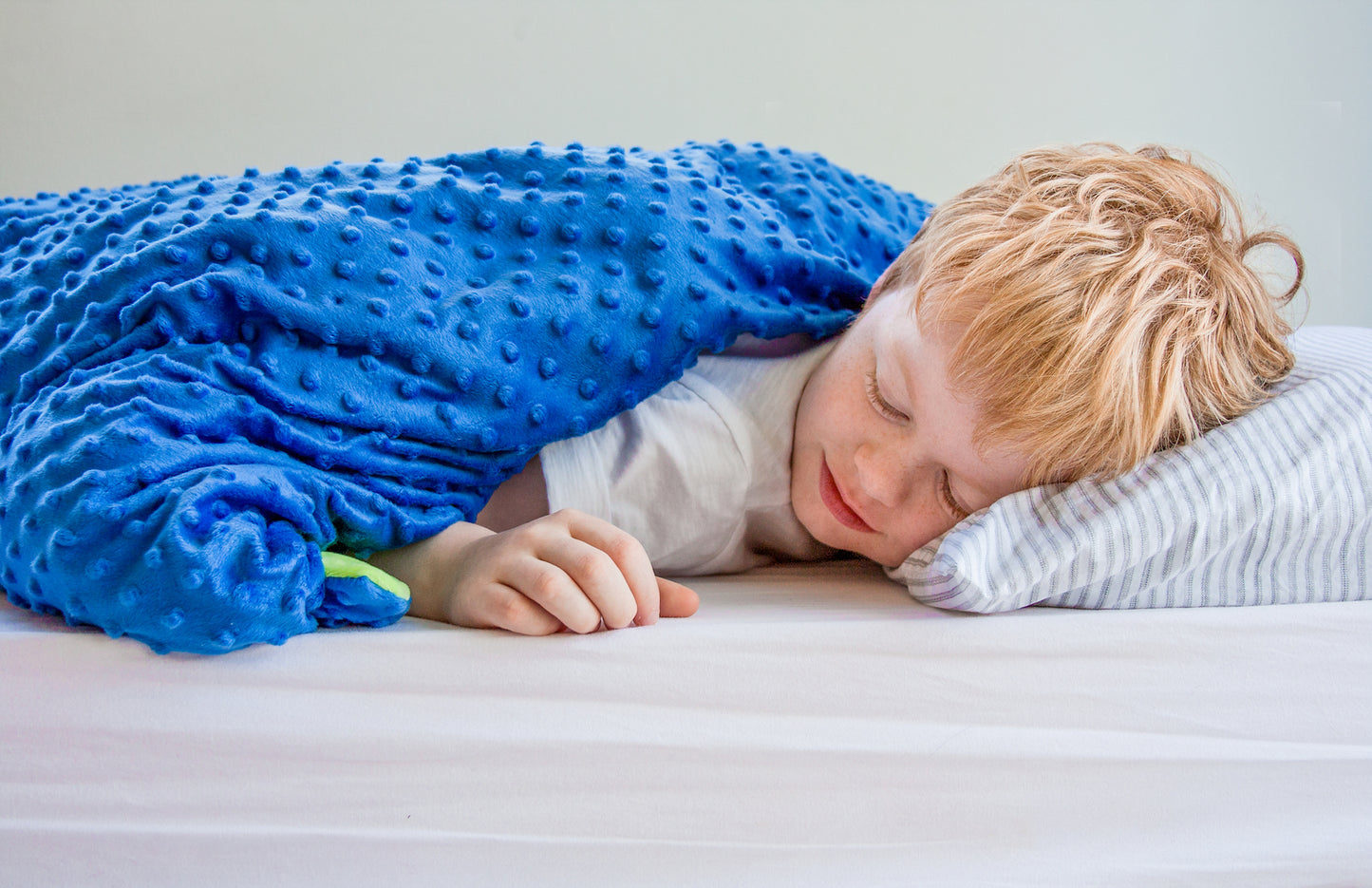 Boy resting under reversible Lottie Dottie Weighted Blanket in blue/green.