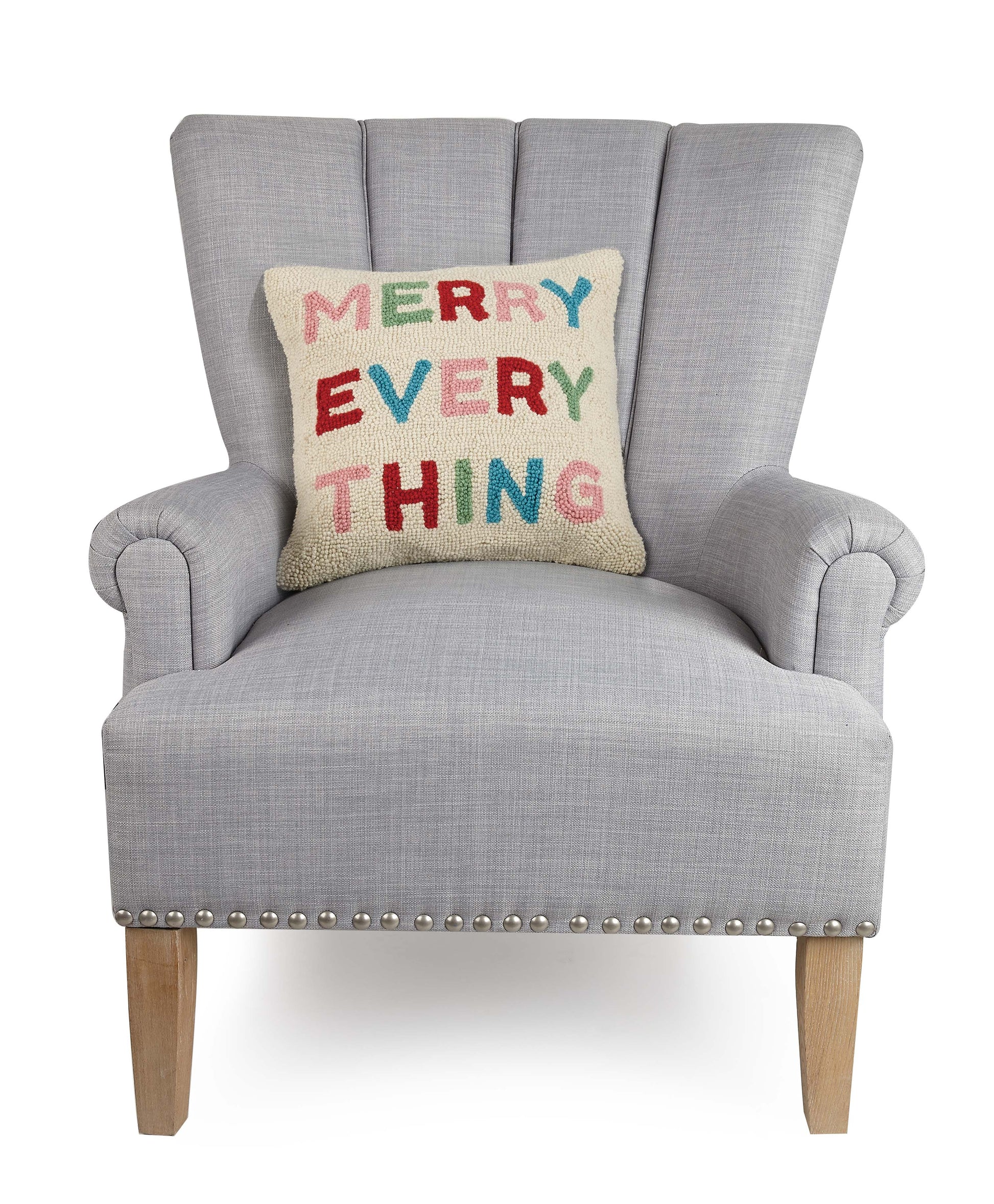 Wool, Holiday hooked pillow with cream background and “Merry Everything” against gray upholstered chair.