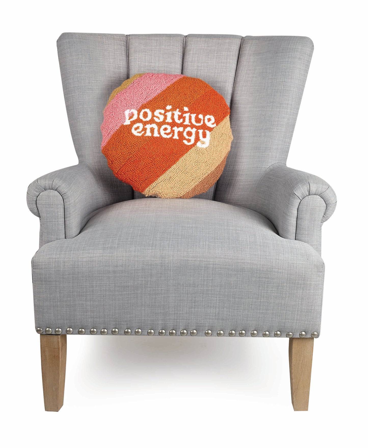 Round, earth-toned, Cat Coq throw pillow that reads, “positive energy” against gray upholstered chair.