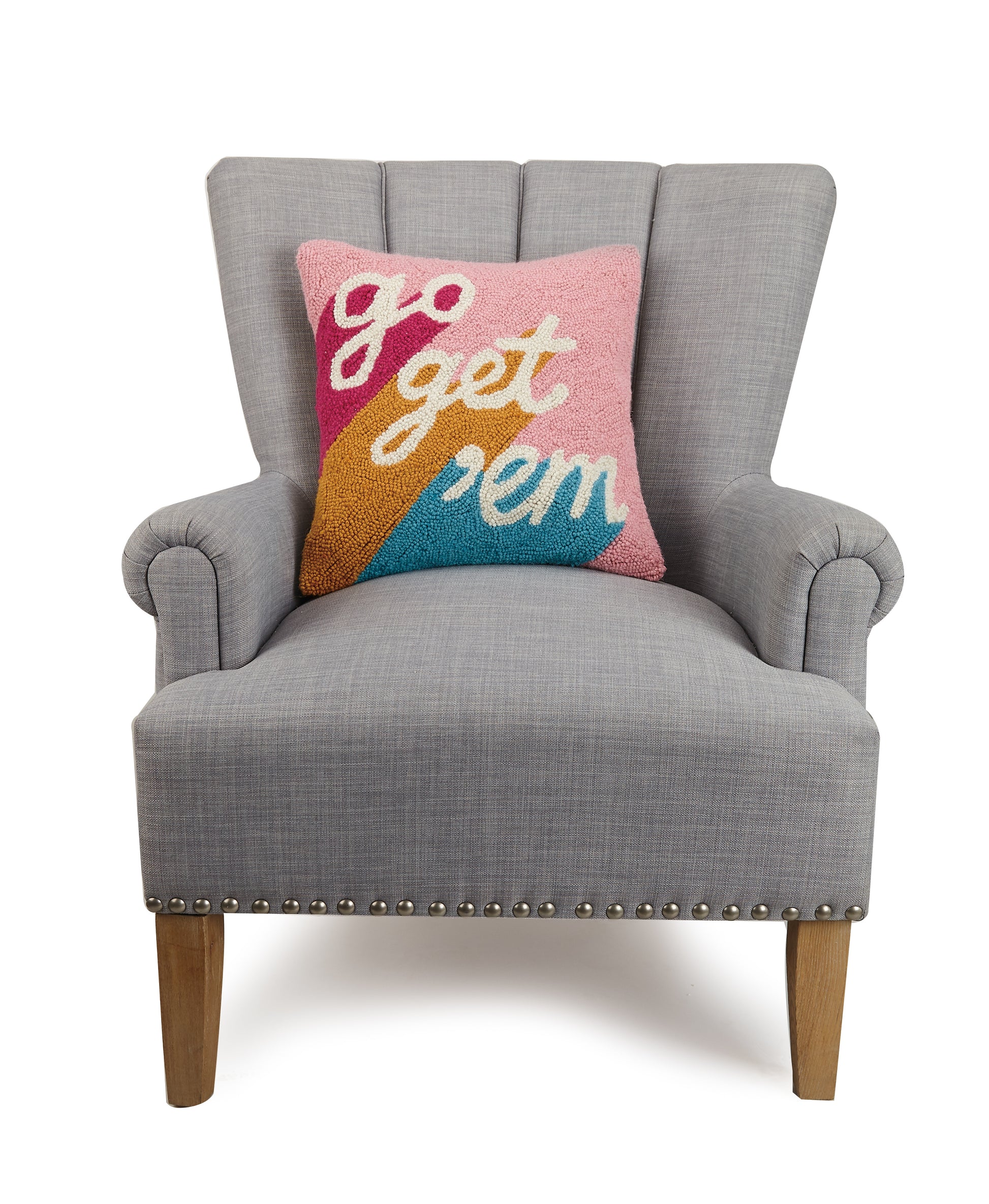 Pink, orange and blue wool hooked throw pillow that reads, “go get ‘em” against gray upholstered chair.