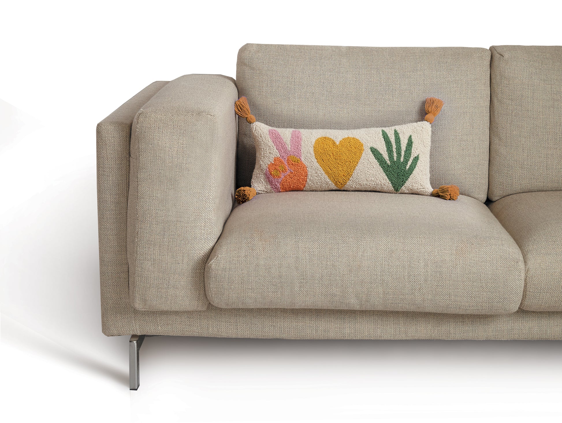 Cream lumbar pillow with peace symbol, heart and plant graphics and golden tassels beige mid-century sofa.