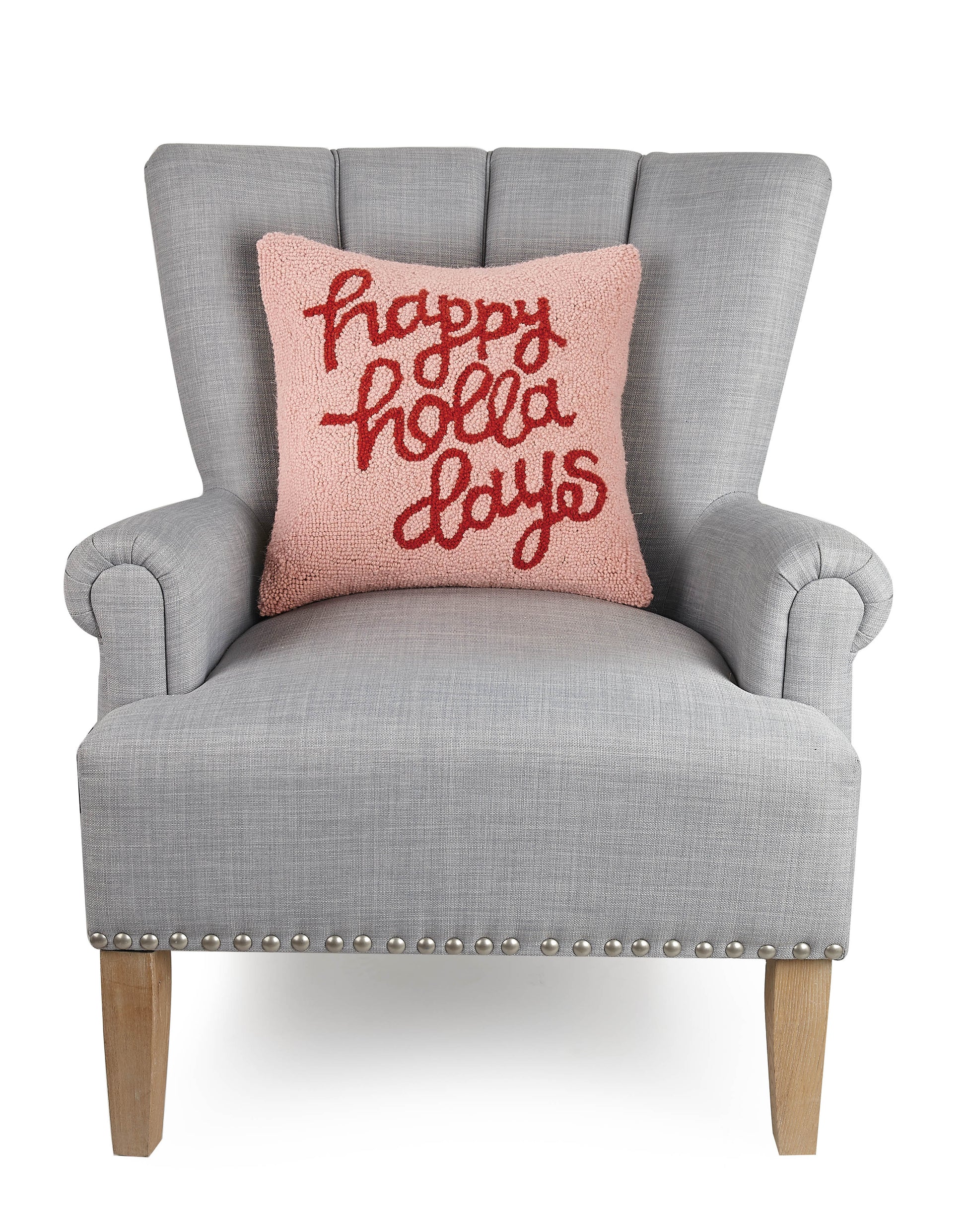 “Happy holla days” wool, holiday throw pillow in pink and red against gray upholstered chair.